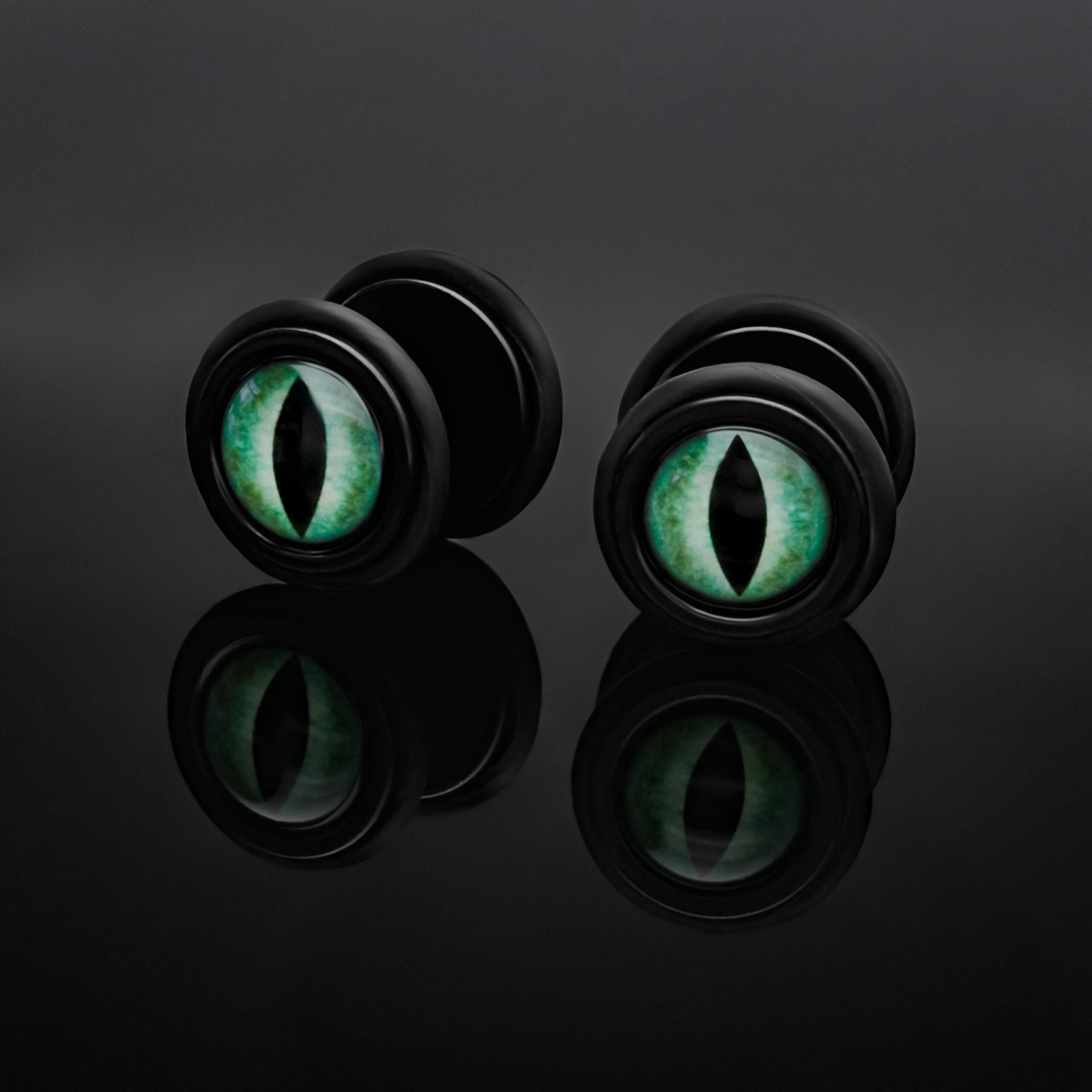 Finti plug neri con occhio di gatto verde su sfondo nero