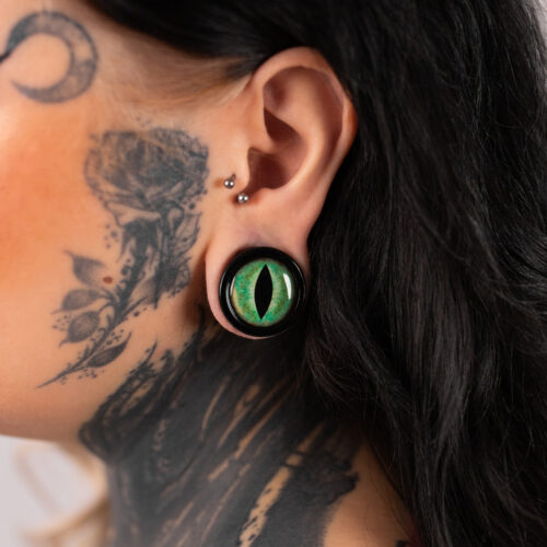 Grande plug occhio di gatto verde nell'orecchio di una persona tatuata
