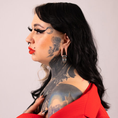 Donna con tatuaggi indossa peso per orecchio nero e argento, abbigliamento rosso