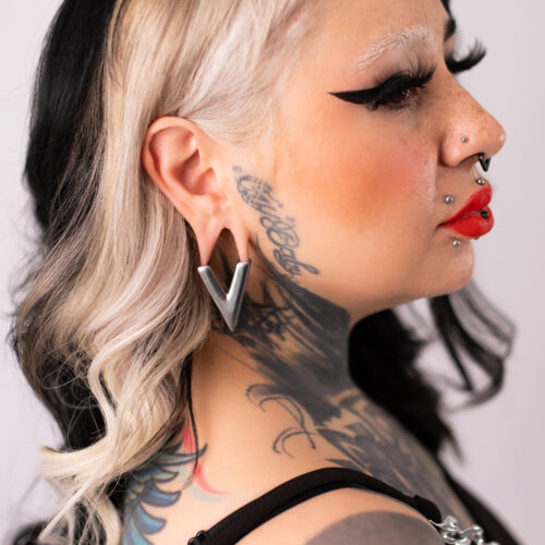 Donna con orecchino a forma di V in argento, capelli neri, collo tatuato