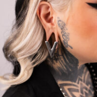 Orecchino a forma di V in argento nell'orecchio di una persona tatuata, profilo laterale