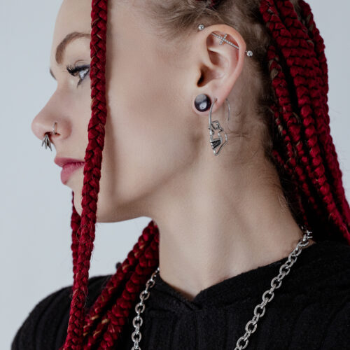 Orecchino a forma di teschio in acciaio chirurgico argentato su un orecchio con trecce rosse