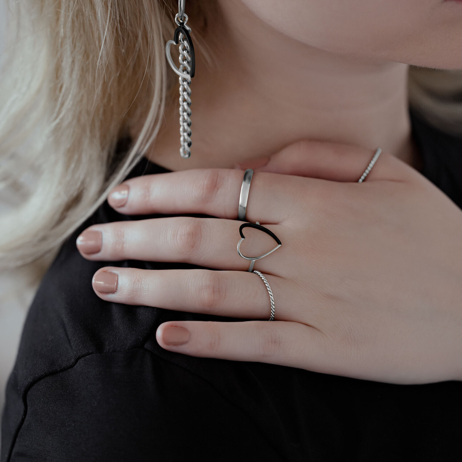 Primo piano di una mano con anello a cuore bicolore in acciaio chirurgico, indossato accanto ad altri anelli