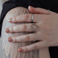 Anello a cuore in argento in acciaio chirurgico su una mano con braccio tatuato