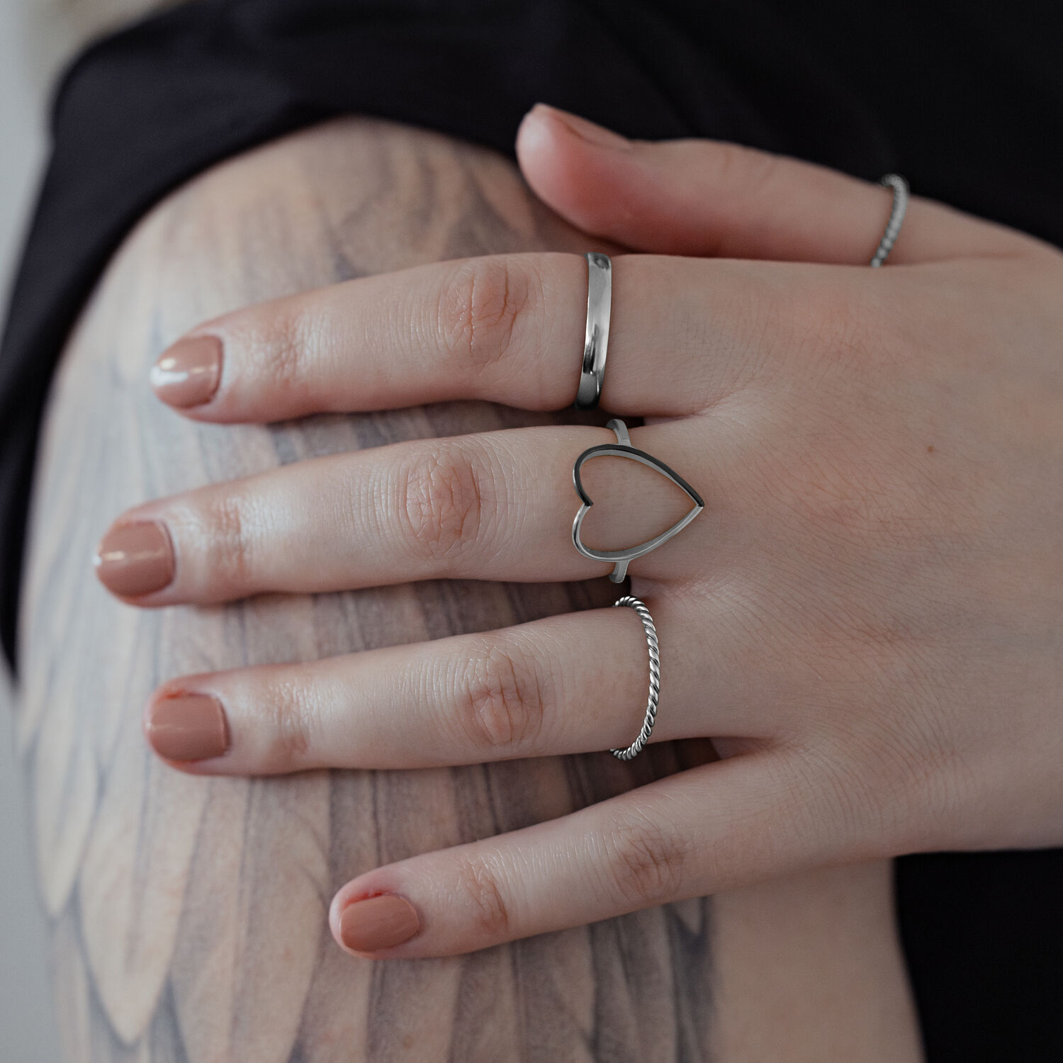 Anello a cuore in argento in acciaio chirurgico su una mano con braccio tatuato