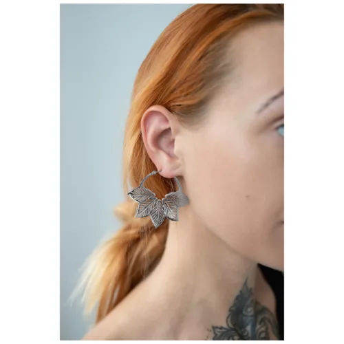 Orecchini d'argento a forma di foglia su un orecchio di una persona con capelli rossi