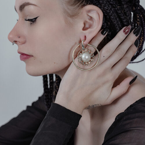 Donna con treccia, indossa grandi pesi per orecchie dorati con onice bianco, mano all'orecchio