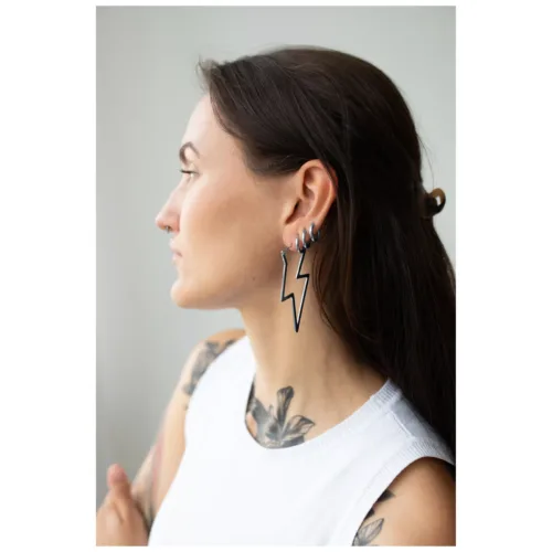 Donna con capelli lunghi indossa orecchini a fulmine neri in acciaio, ritratto laterale