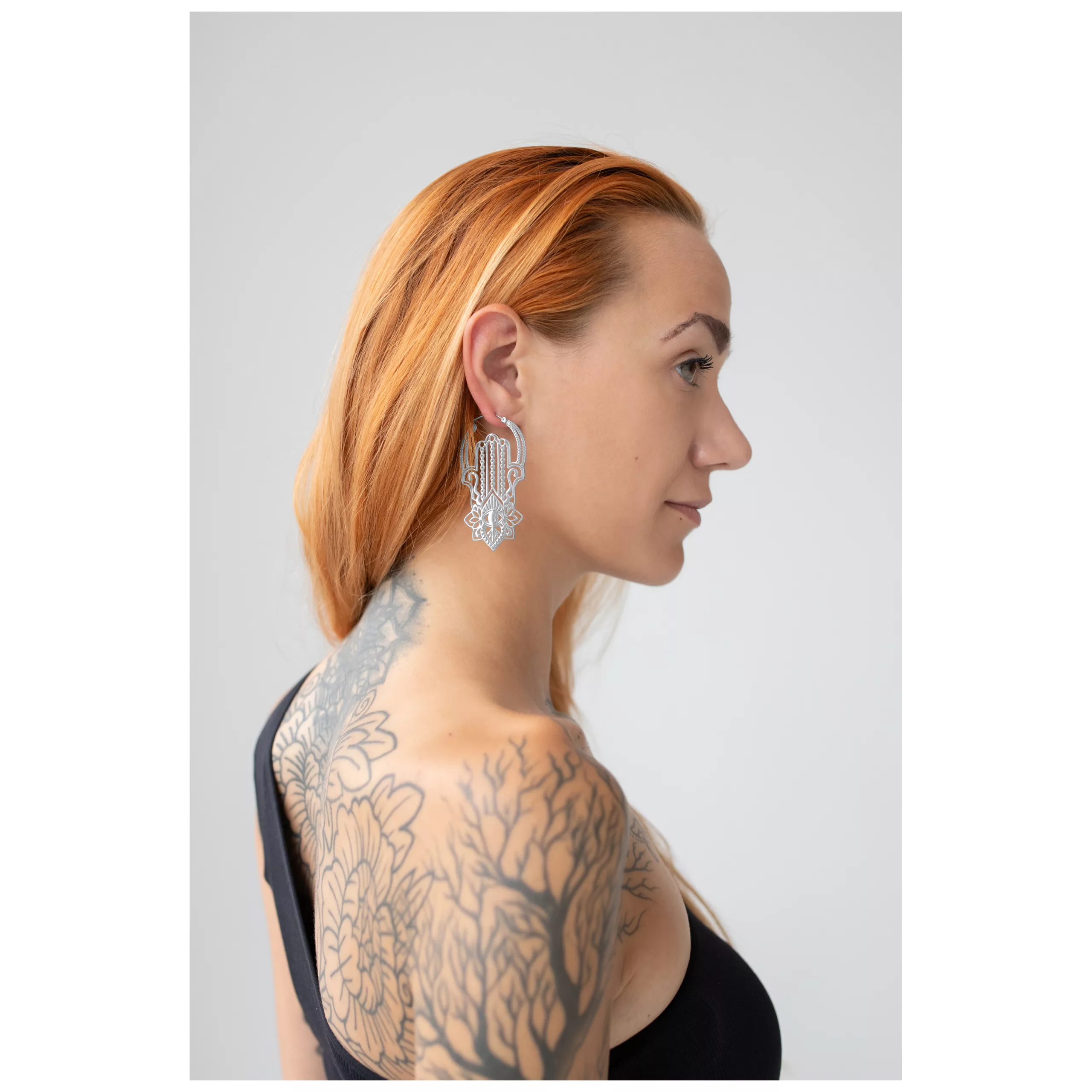Donna con lunghi capelli castano-rossicci indossa orecchini Khamsa Hoops in argento su sfondo neutro