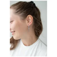 Donna indossa orecchini a croce in argento, sorridente di profilo su sfondo chiaro