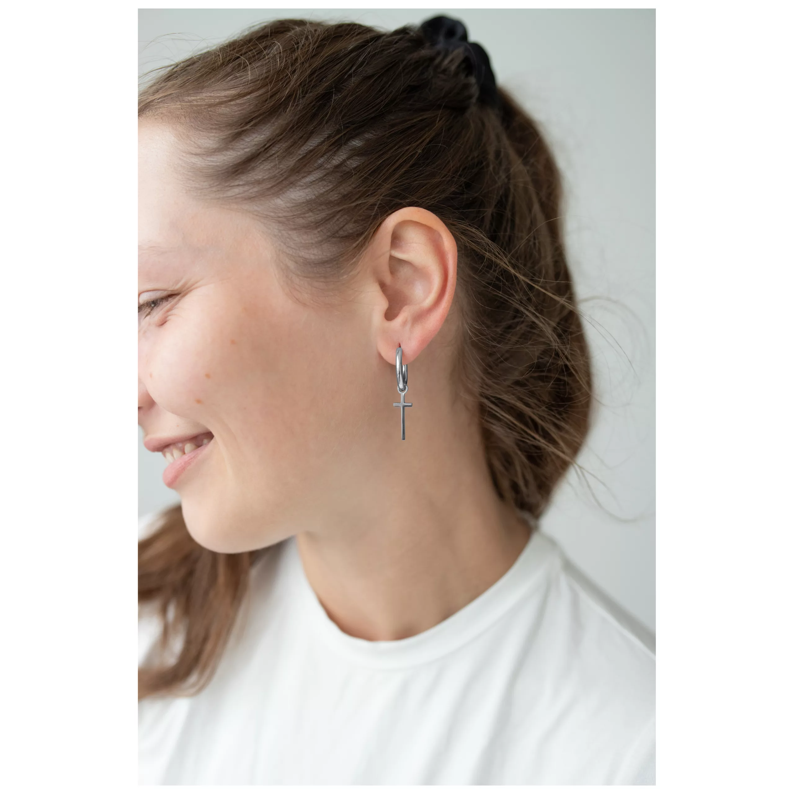 Donna indossa orecchini a croce in argento, sorridente di profilo su sfondo chiaro