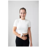 Donna con top bianco e pantaloni neri indossa Little Cross Hoops in argento su sfondo bianco