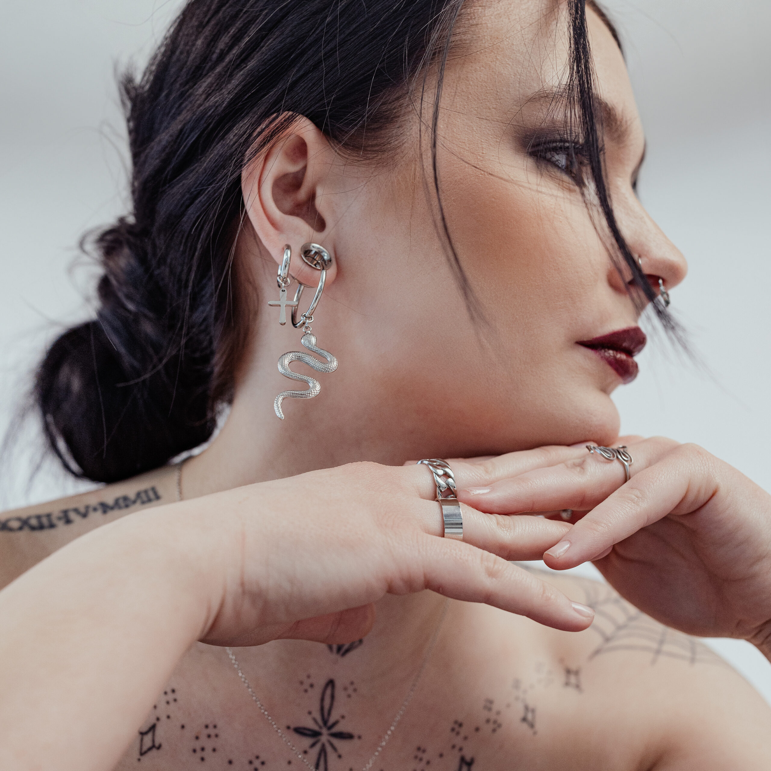 Donna con orecchini Little Cross Hoops in argento e orecchino a serpente, sfondo bianco