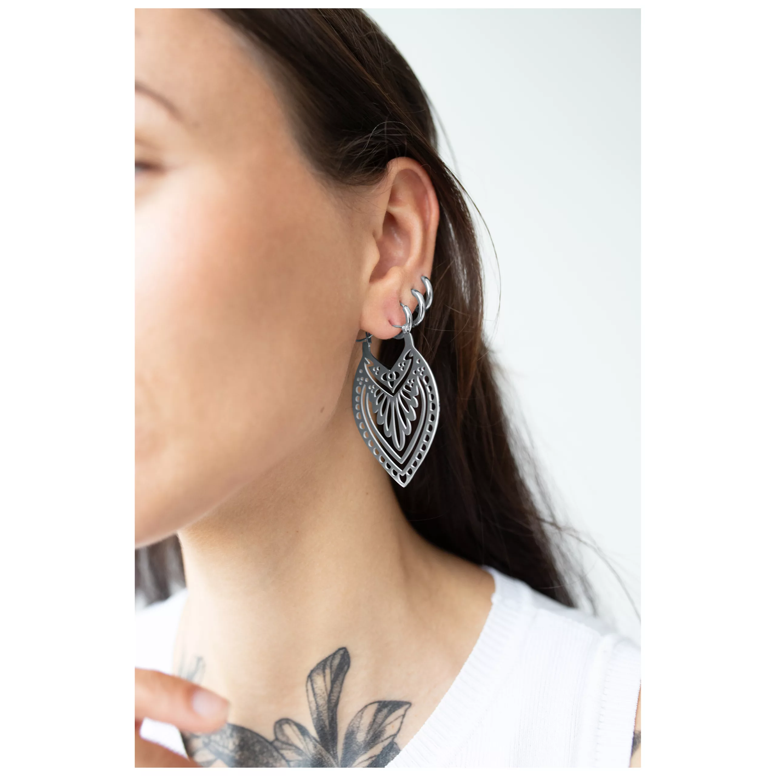 Donna con orecchini Creek Hoops in argento, indossati all'orecchio, sfondo bianco