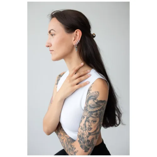 Donna con capelli lunghi e braccia tatuate, indossa orecchini Little Anchor Hoops in argento