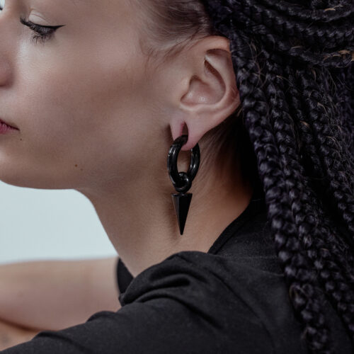 Primo piano di una persona con pesi per orecchie Arrow neri in acciaio chirurgico, capelli intrecciati sullo sfondo