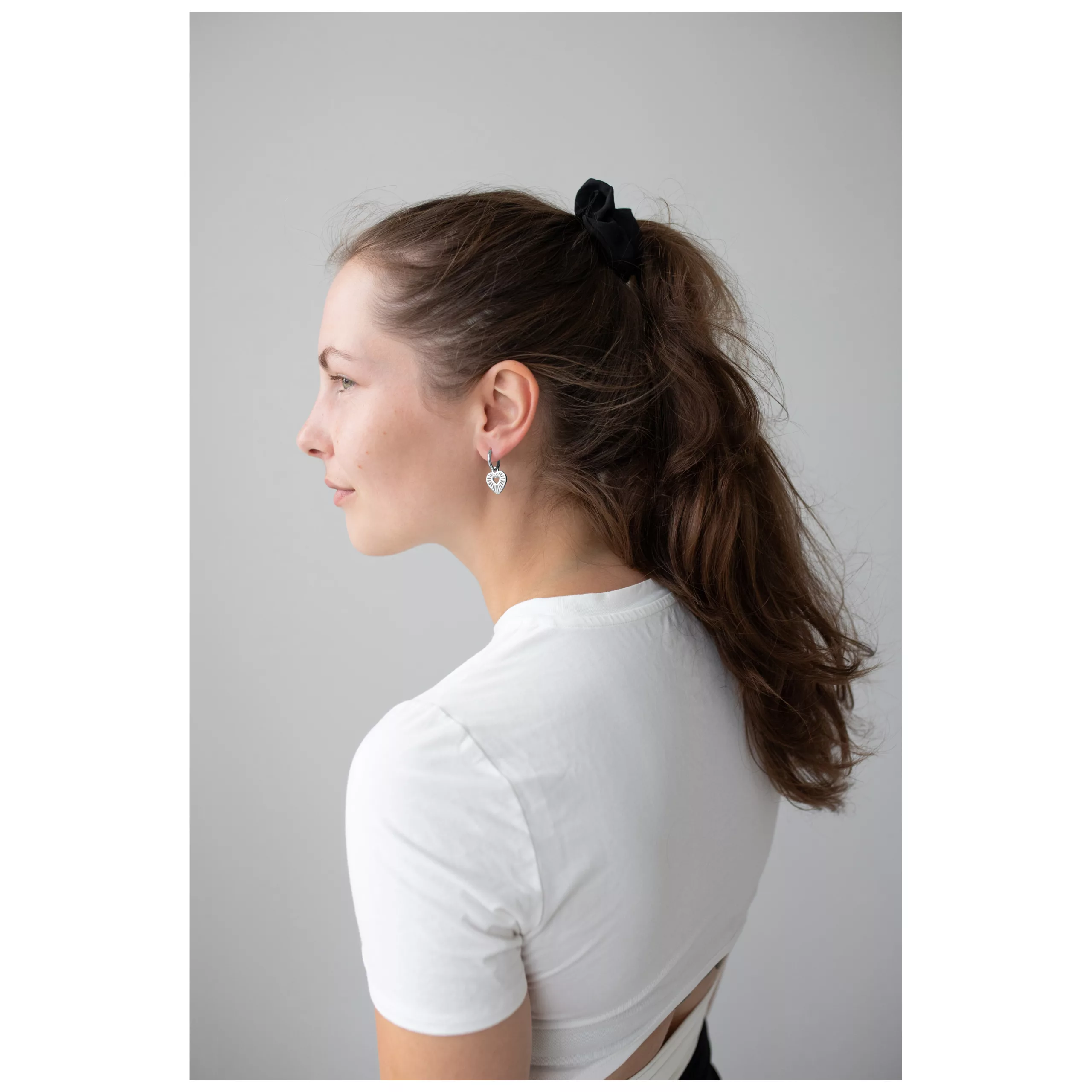 Donna con maglietta bianca indossa cerchi a cuore in argento su sfondo grigio