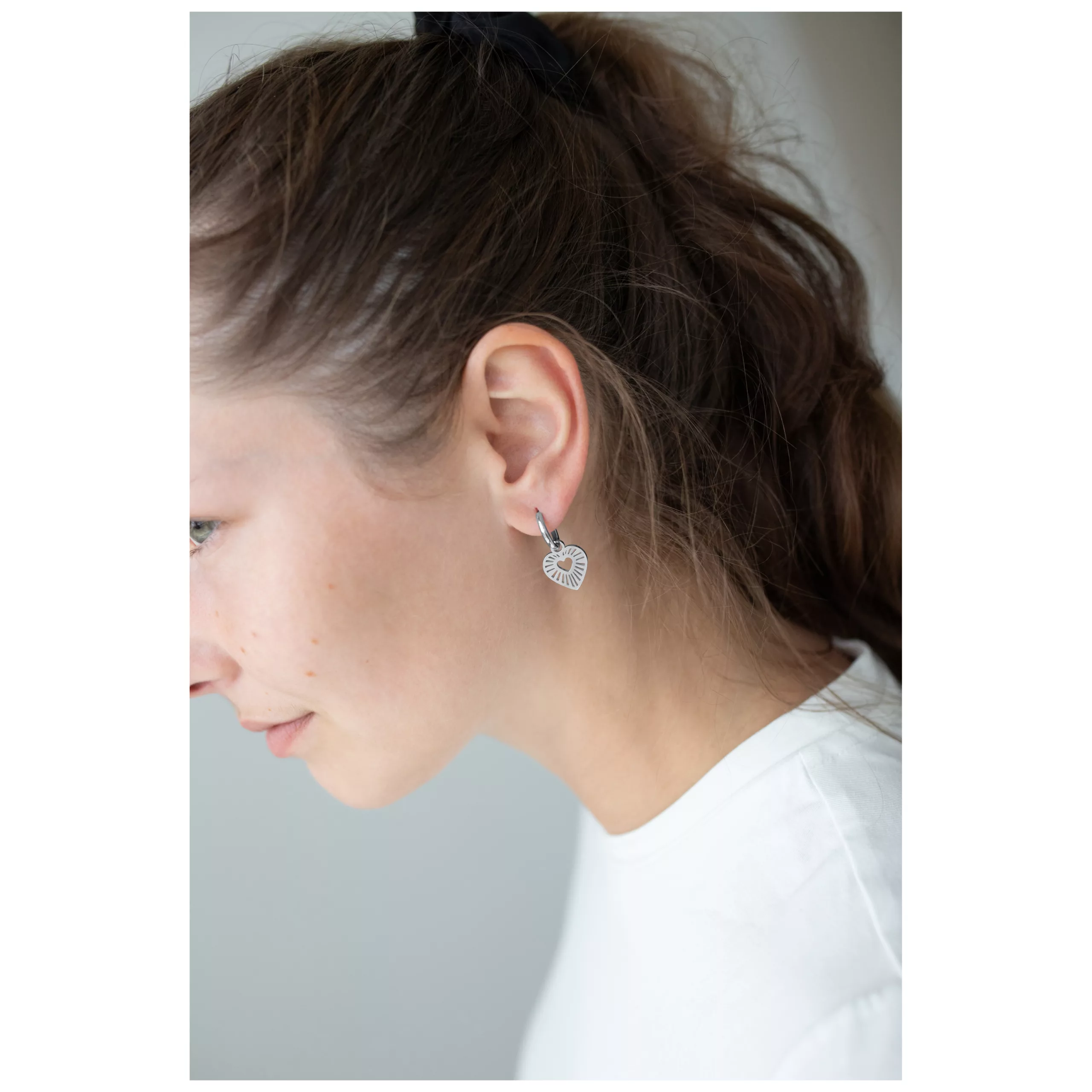 Donna che indossa orecchini a cerchio a forma di cuore in argento, fotografata di lato, con sfondo bianco