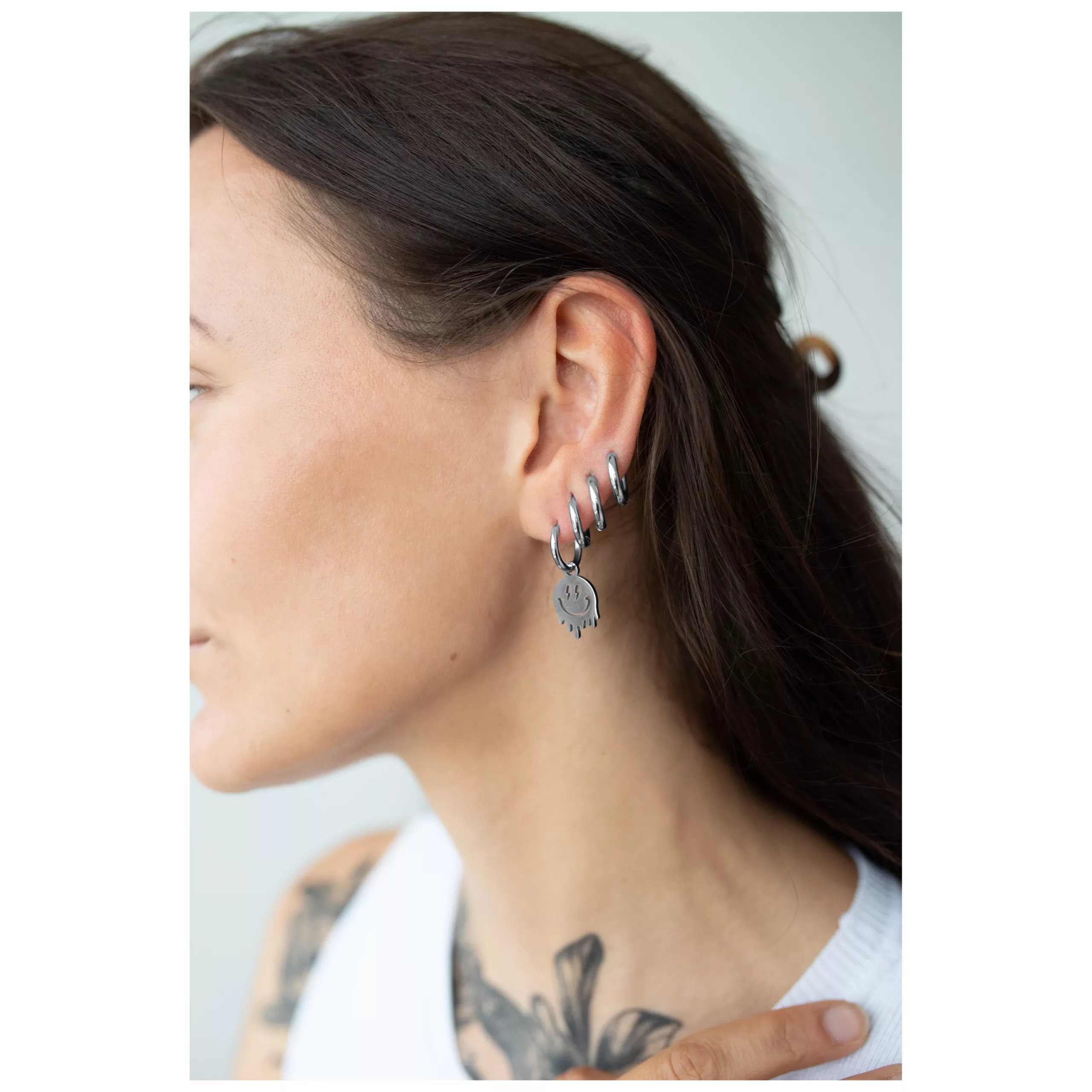 Donna con capelli lunghi indossa i Little Smiley Hoops in argento all'orecchio.