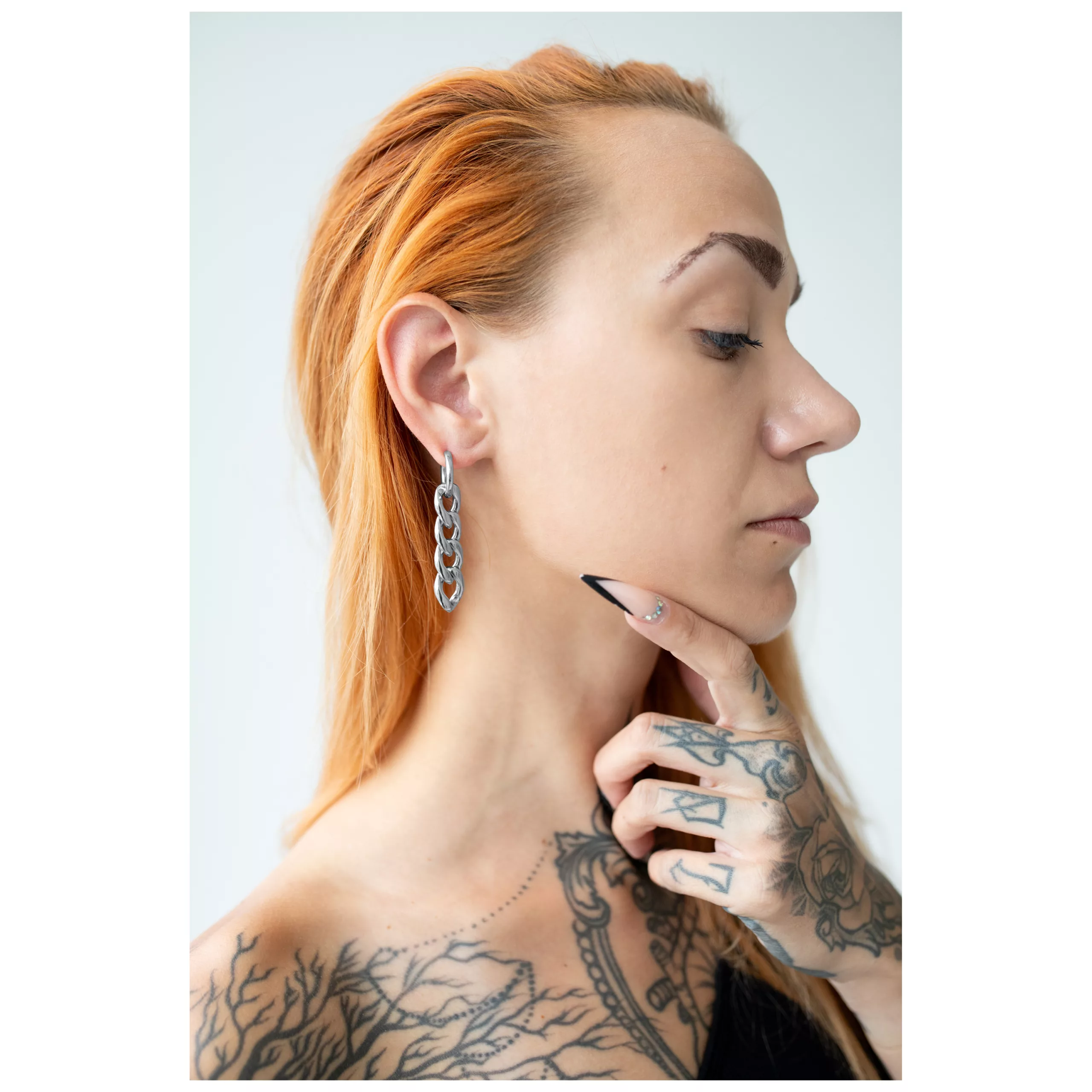 Orecchini in argento con design a catena indossati su un orecchio con mano tatuata e capelli rossi