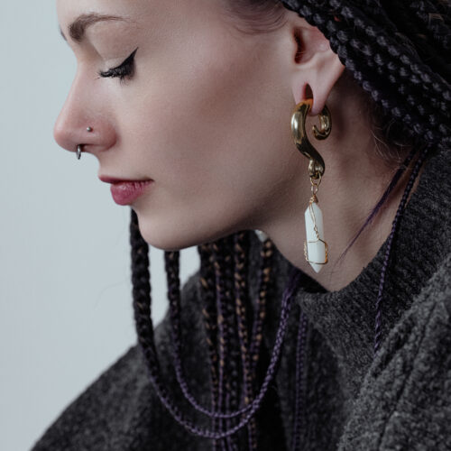 Donna con capelli intrecciati indossa pesi per orecchie dorati con pietre bianche.