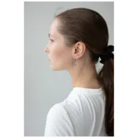 Donna con coda di cavallo laterale indossa piccoli orecchini a cerchio triangolari neri e argento su sfondo grigio