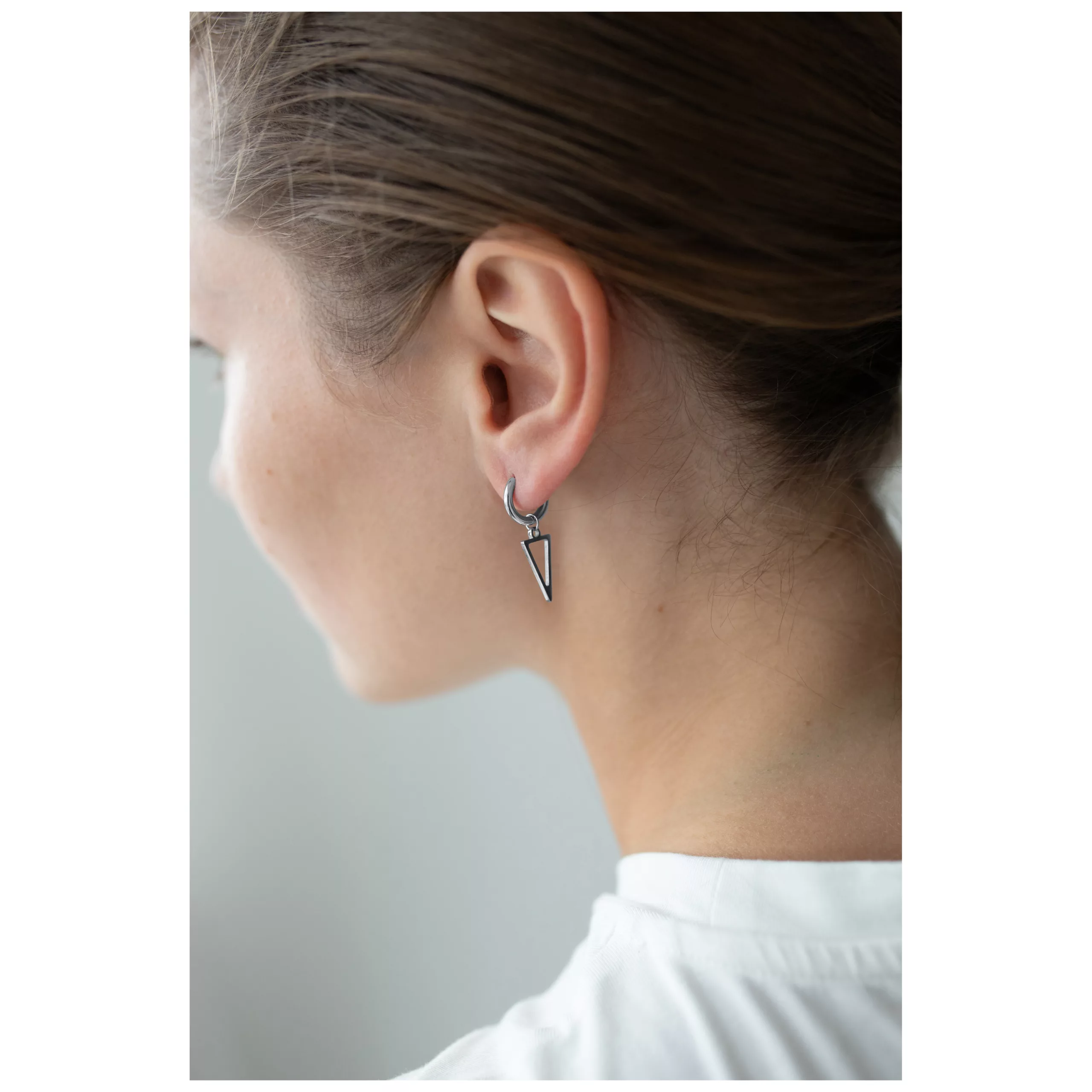Orecchini a cerchio triangolari neri e argento sull'orecchio di una persona con capelli castani, sfondo bianco