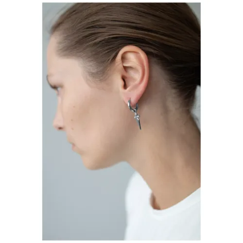 Donna con piccoli orecchini a croce in acciaio chirurgico nero-argento su sfondo grigio