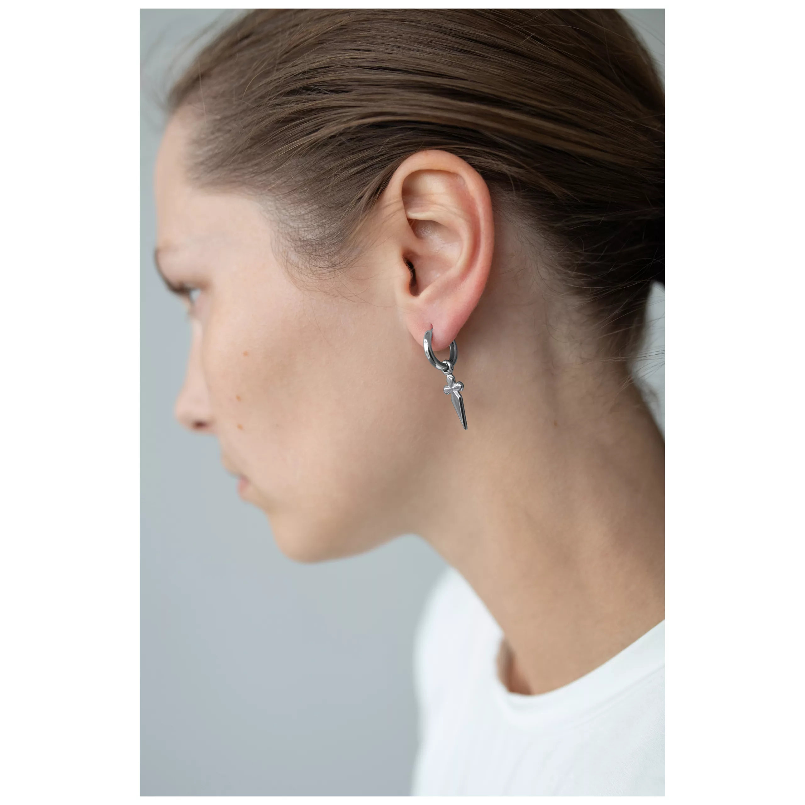 Donna con piccoli orecchini a croce in acciaio chirurgico nero-argento su sfondo grigio