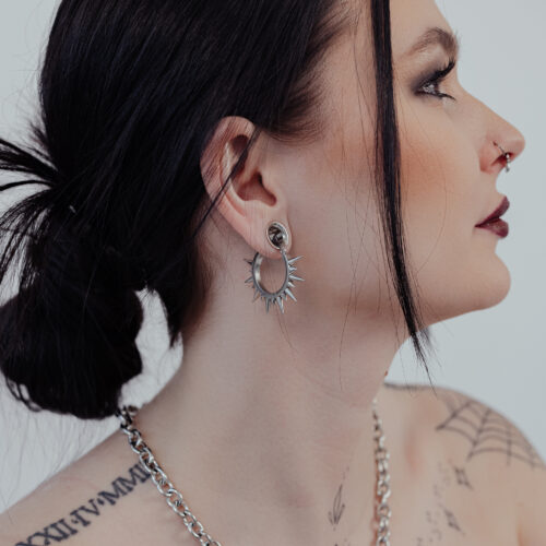 Donna con capelli neri indossa orecchini spinosi argentati su sfondo chiaro