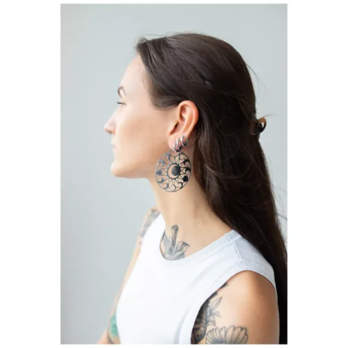 Donna con lunghi capelli scuri indossa grandi orecchini rotondi con motivo lunare su sfondo grigio