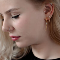 Donna con vari piercing, incluso un piercing in cristallo dorato all'orecchio.