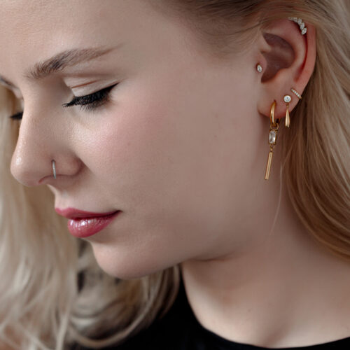 Donna con vari piercing, incluso un piercing in cristallo dorato all'orecchio.