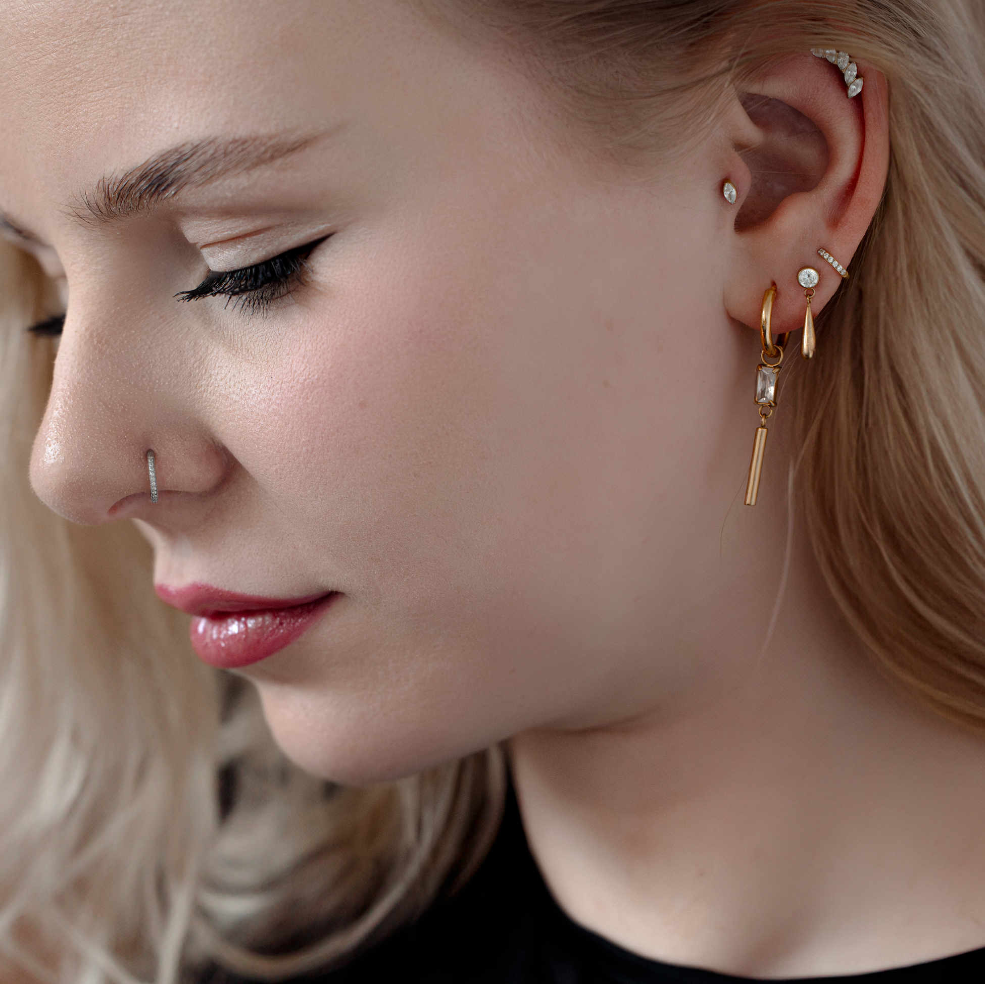 Donna con vari piercing, incluso un piercing in cristallo dorato all'orecchio.