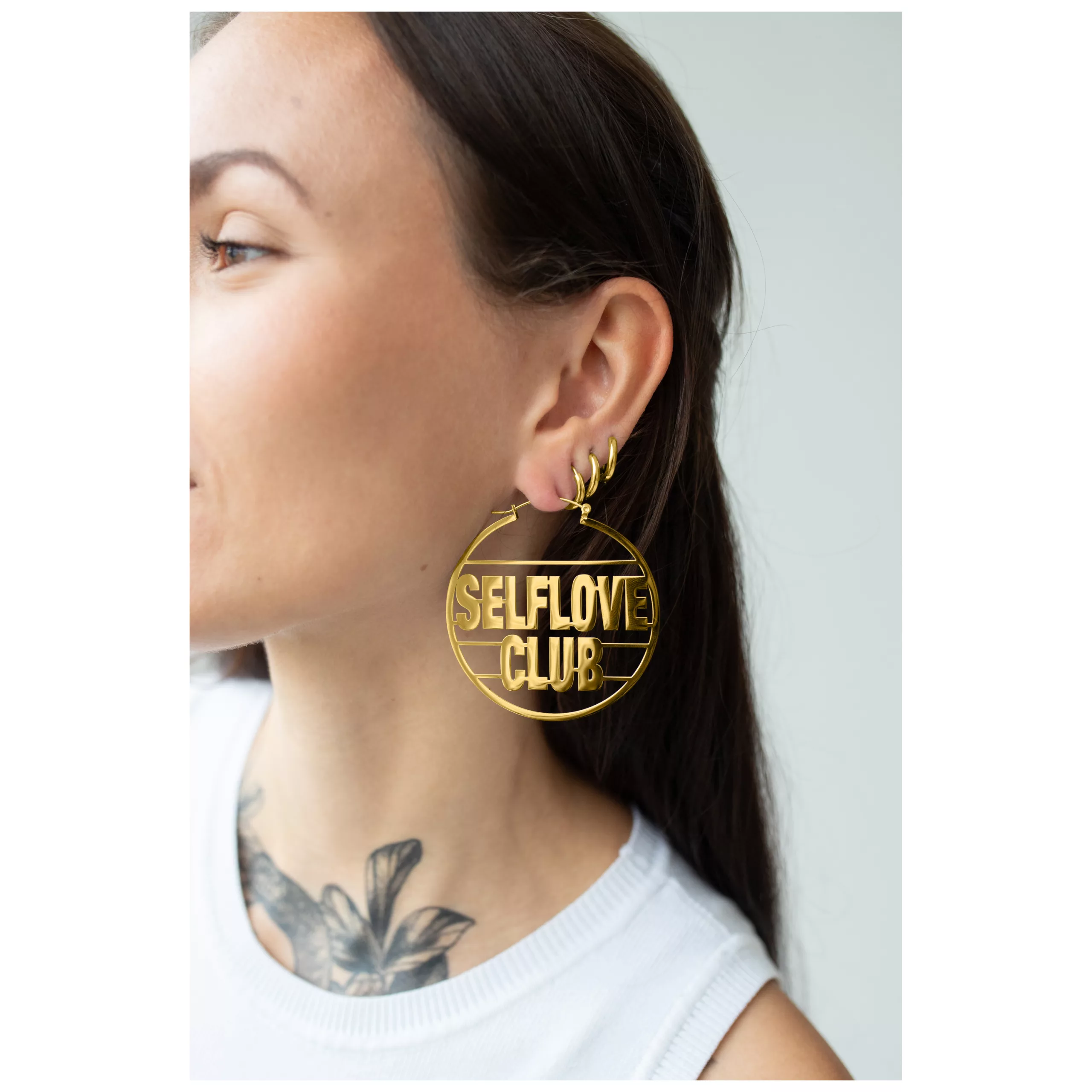 Donna indossa grandi orecchini d'oro con scritta 'Selflove Club'