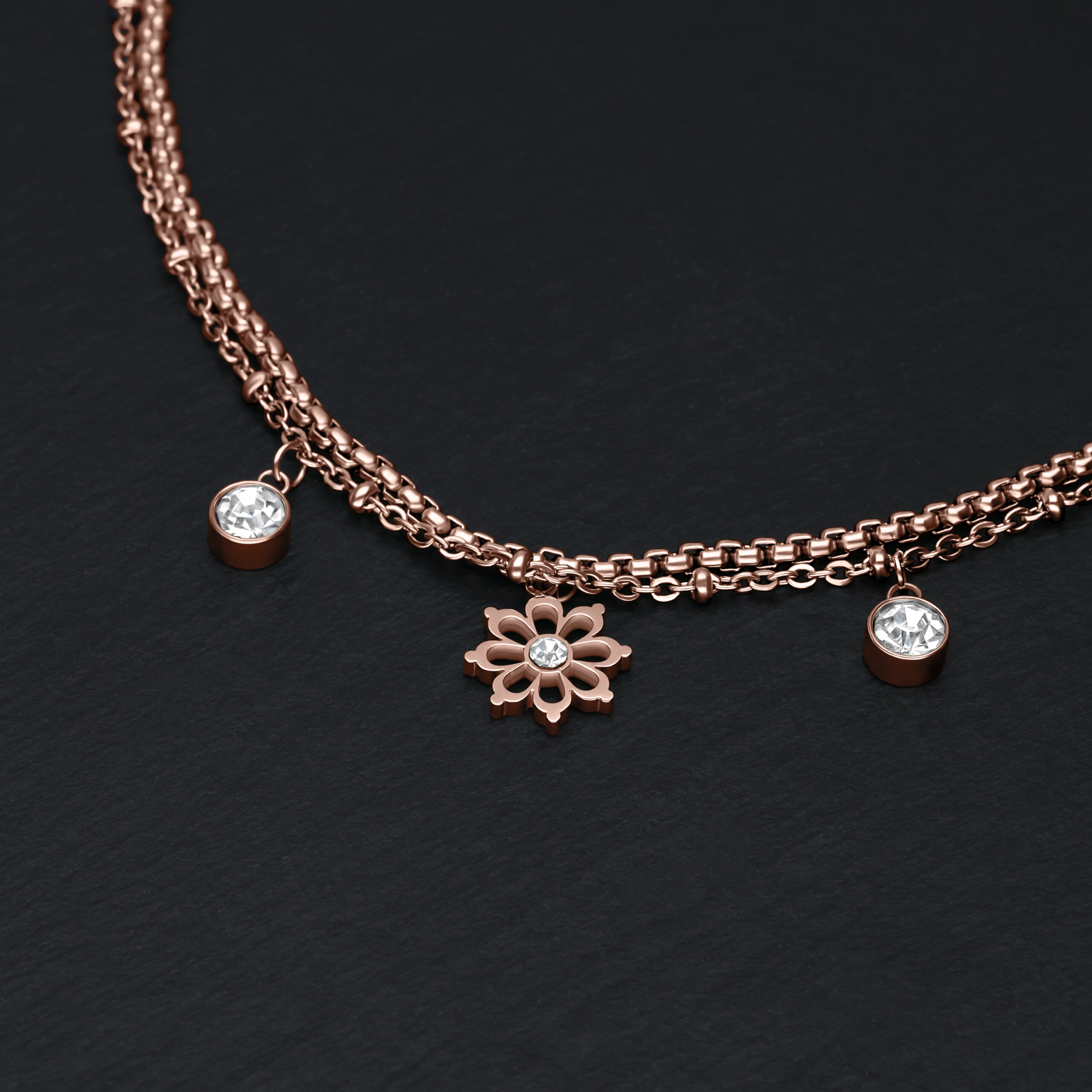 Bracciale in oro rosa con ciondolo a forma di fiore e cristalli chiari su sfondo nero