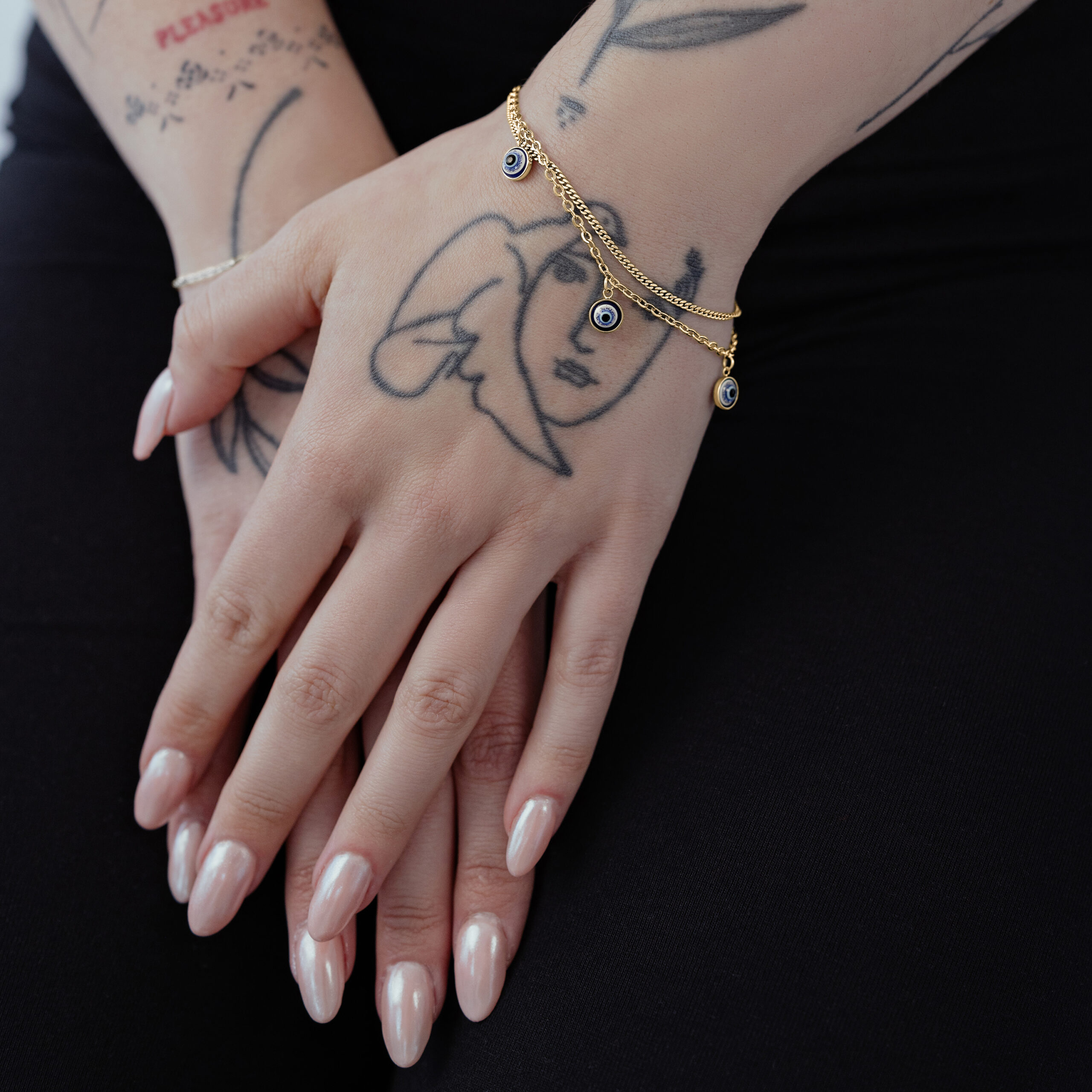 Braccialetto Little Nazar dorato su un polso tatuato su sfondo nero
