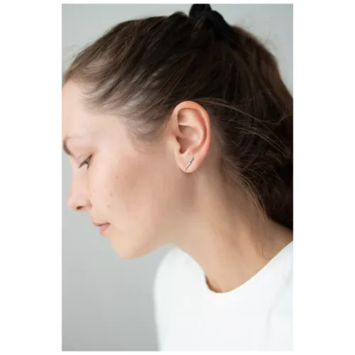 Orecchini d'argento con cristalli sull'orecchio di una donna su sfondo neutro