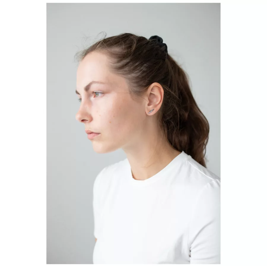 Donna con capelli castani indossa discreti orecchini d'argento su sfondo grigio