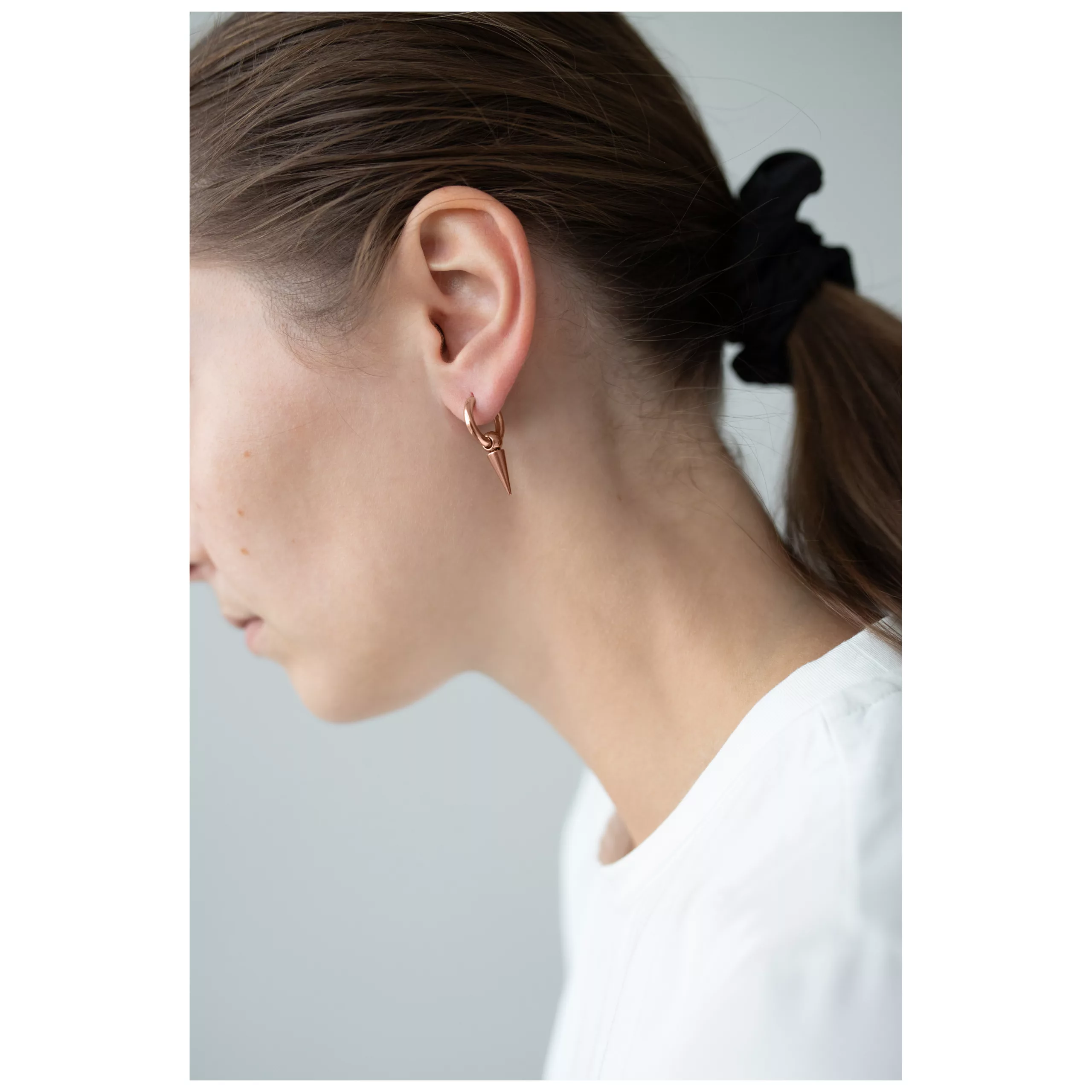 Primo piano di un orecchio con orecchini a spillo in oro rosa e elastico nero per capelli