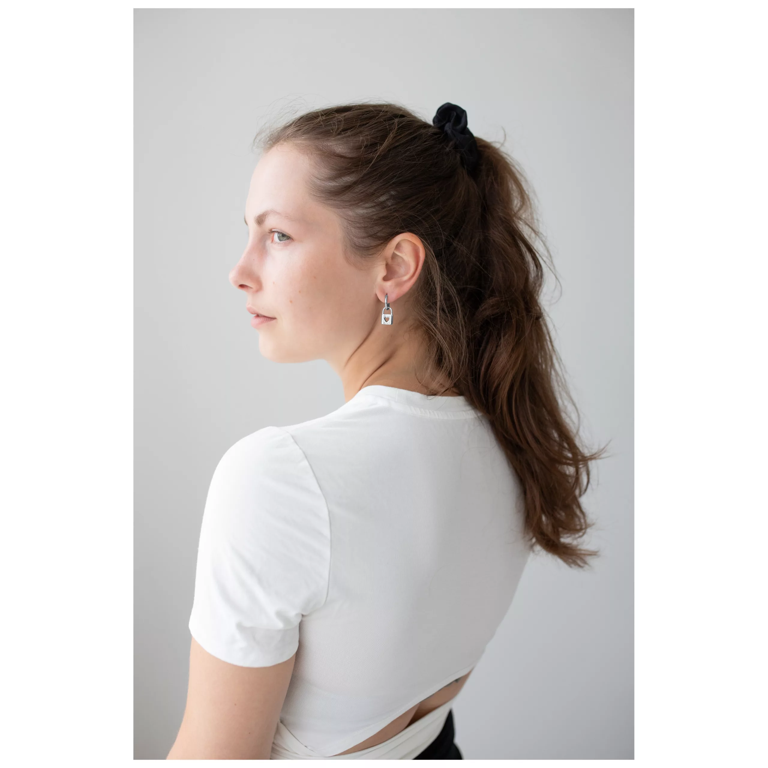 Donna con capelli lunghi indossa orecchini Little Lock Hoops in argento su sfondo bianco