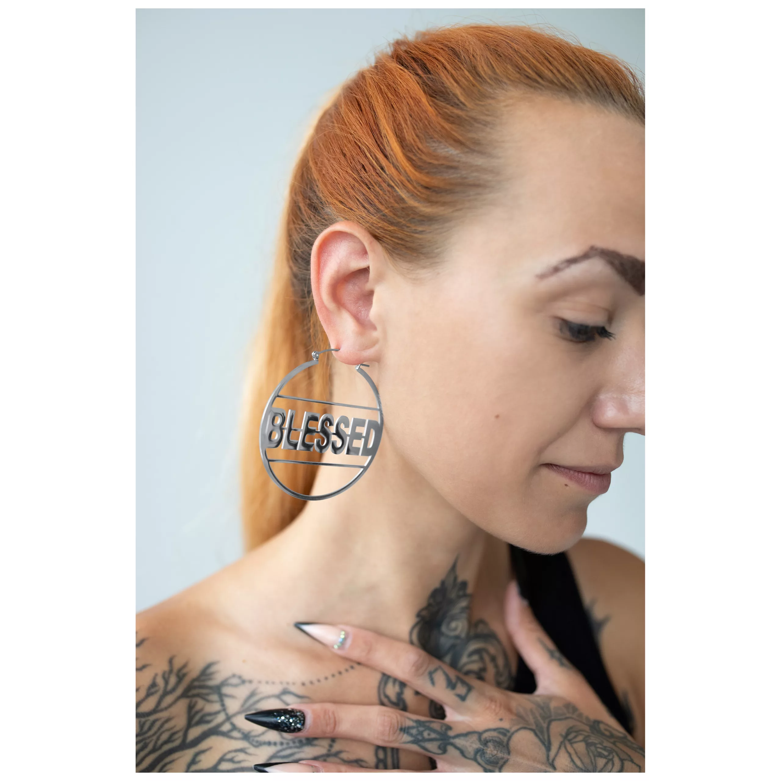 Orecchini Blessed Hoops d'argento in acciaio inossidabile, all'orecchio di una donna, su sfondo neutro
