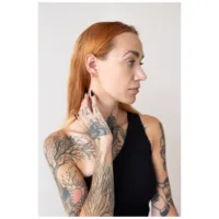 Persona con braccio tatuato indossa orecchini Little Bar Hoops in oro rosa
