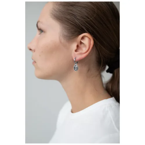 Vista laterale di una donna con orecchini a croce in argento su sfondo chiaro