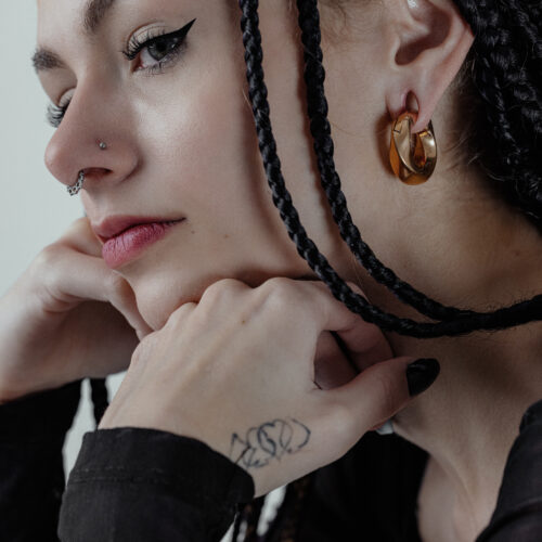 Donna con pesi per orecchie Twisted in oro e trecce su sfondo grigio