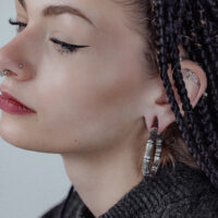 Donna con capelli neri intrecciati indossa un orecchino a peso Bonechain in argento all'orecchio