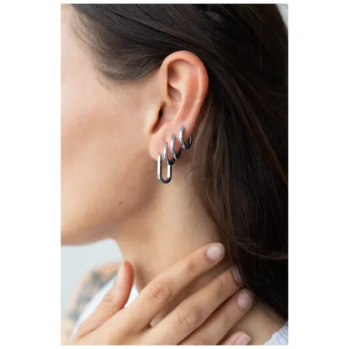 Primo piano di orecchini ovali in nero e argento su un orecchio, mano che tocca il mento