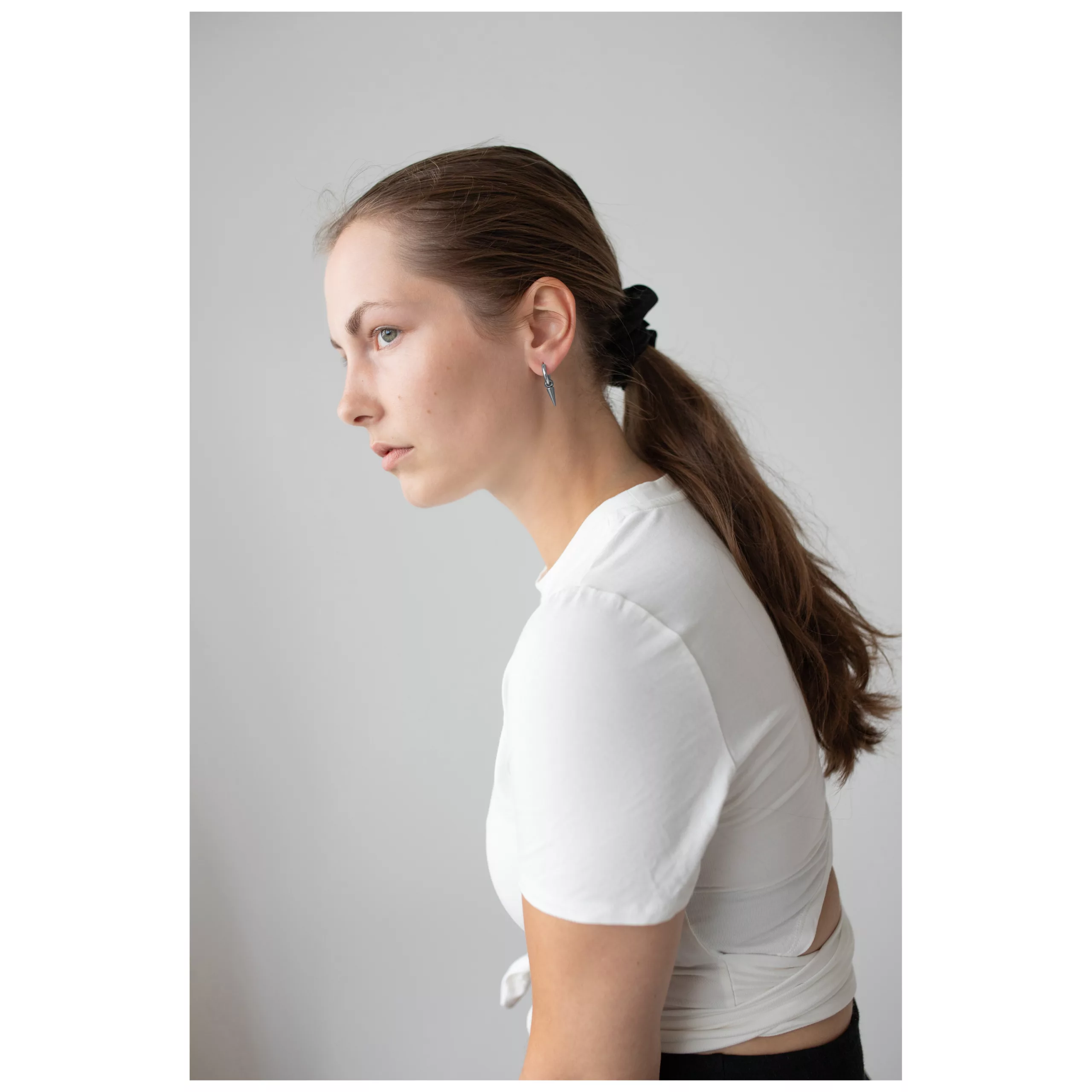 Donna con capelli lunghi e lisci indossa orecchini Spike in acciaio chirurgico nero e argento, top bianco.