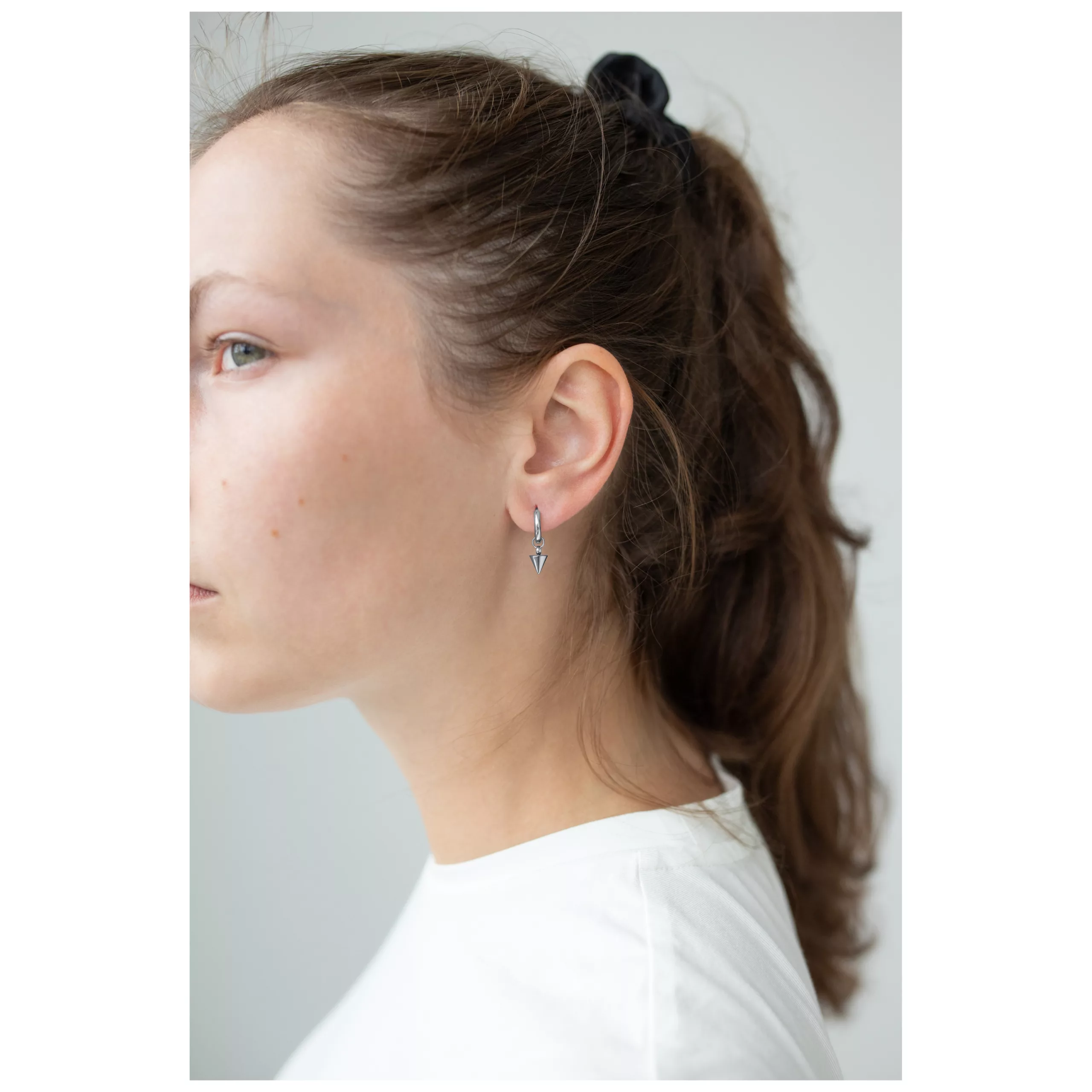 Donna indossa piccoli orecchini a cerchio neri con punte, sfondo bianco