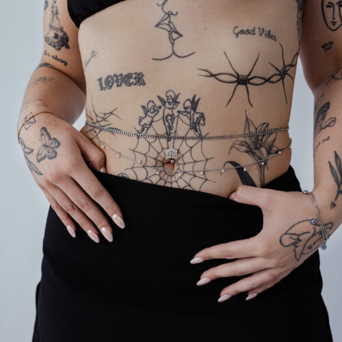 Donna con doppie catene da pancia in acciaio chirurgico, tatuaggi visibili, gonna nera